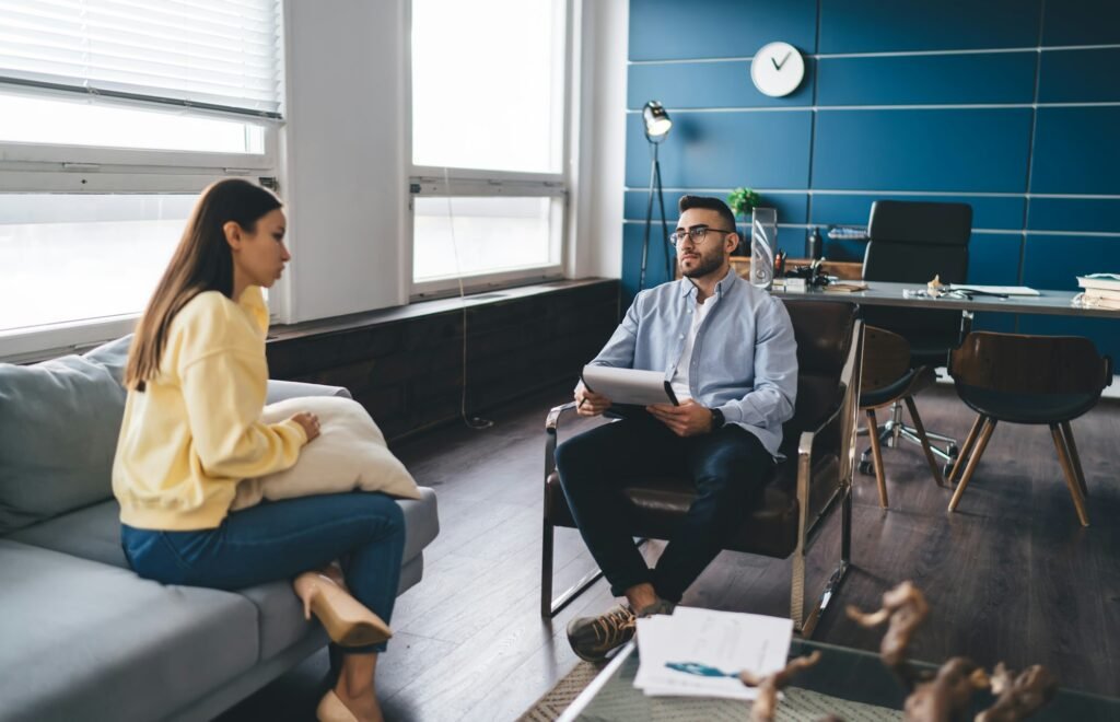 Female patient sitting on sofa during therapy session with psychologist