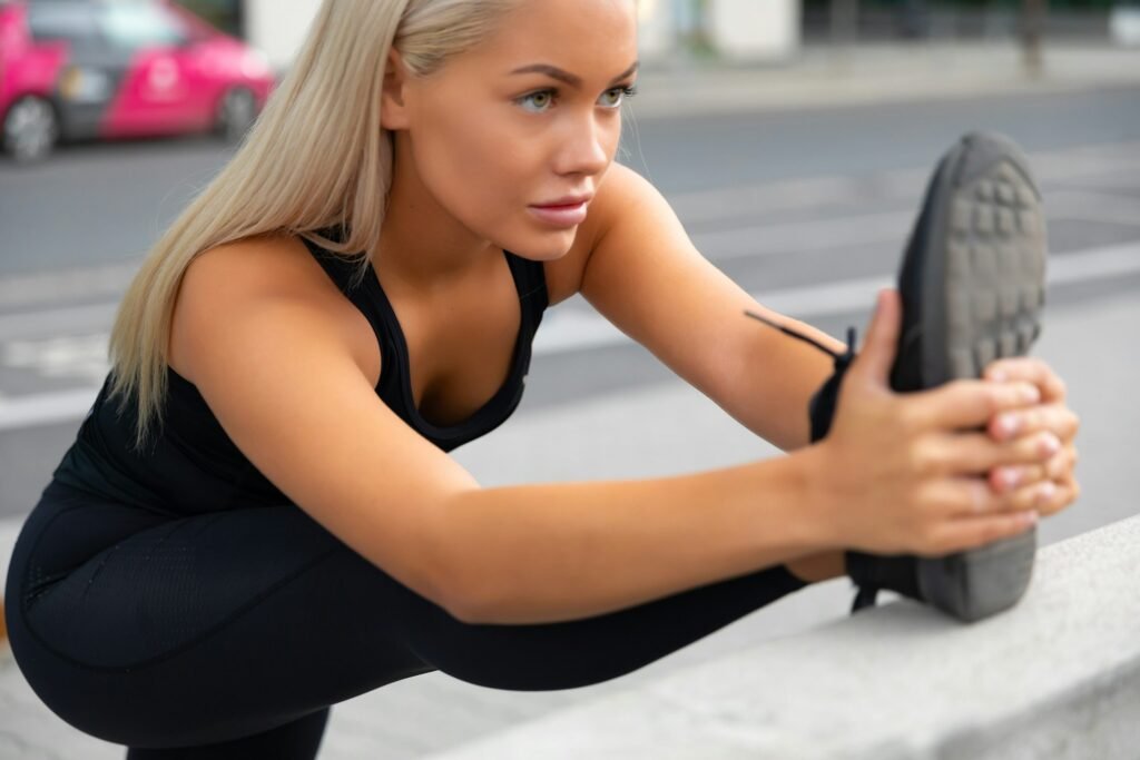 Focused Female Athlete Stretching Leg On Railing At Sidewalk