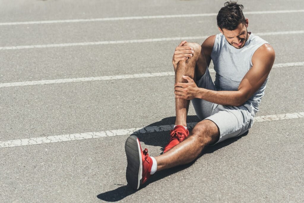 suffering young runner with leg injury sitting on floor of running track