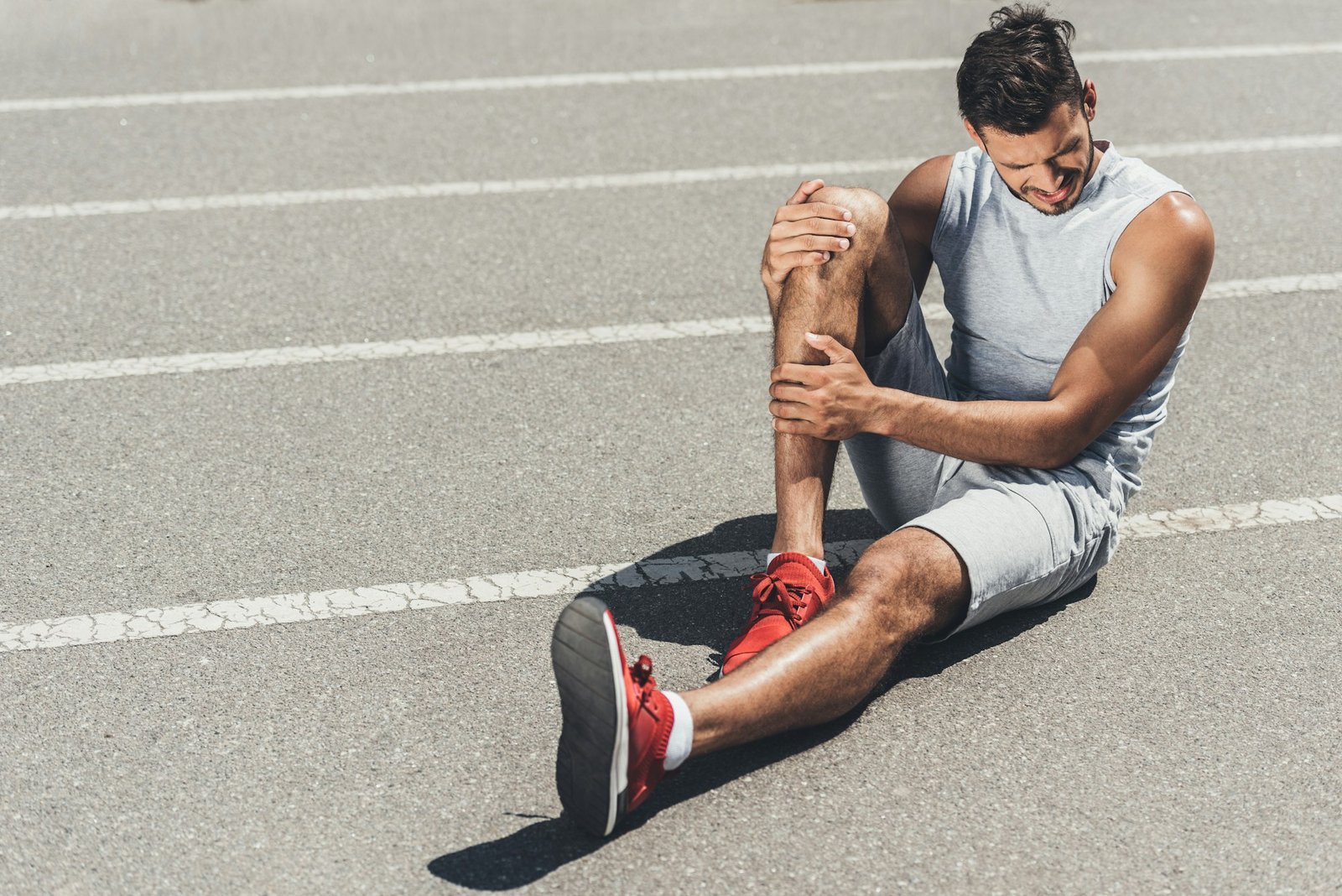 suffering young runner with leg injury sitting on floor of running track